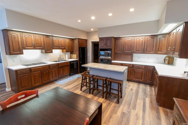 kitchen featuring a breakfast bar, black appliances, sink, light hardwood / wood-style flooring, and a kitchen island