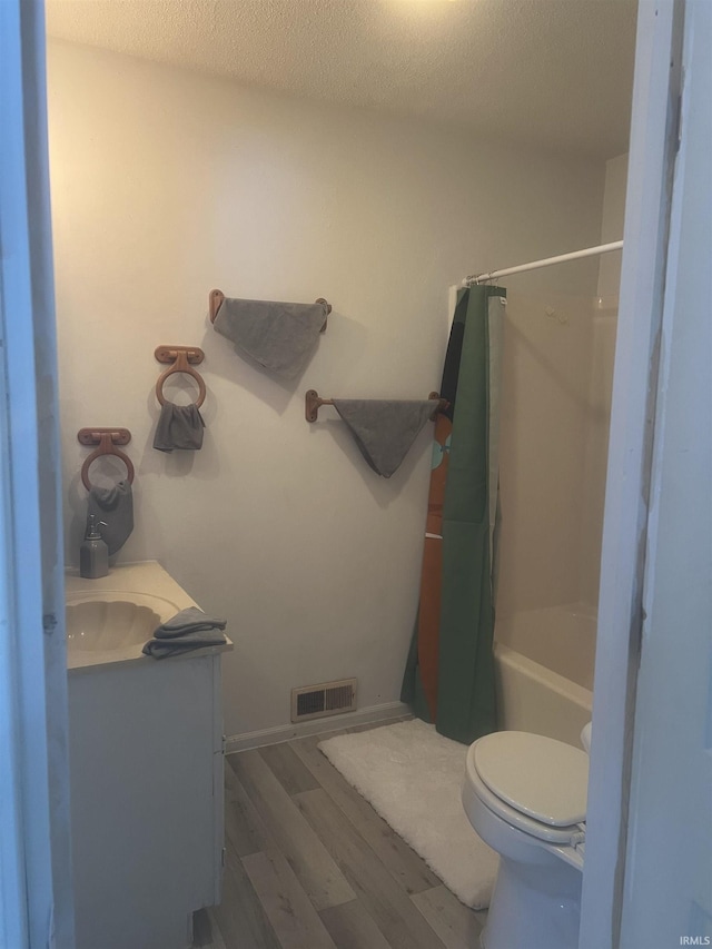 full bathroom featuring hardwood / wood-style floors, vanity, toilet, shower / bath combo with shower curtain, and a textured ceiling