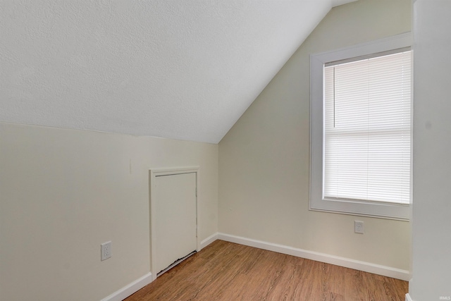 additional living space featuring lofted ceiling, light wood-type flooring, and a textured ceiling