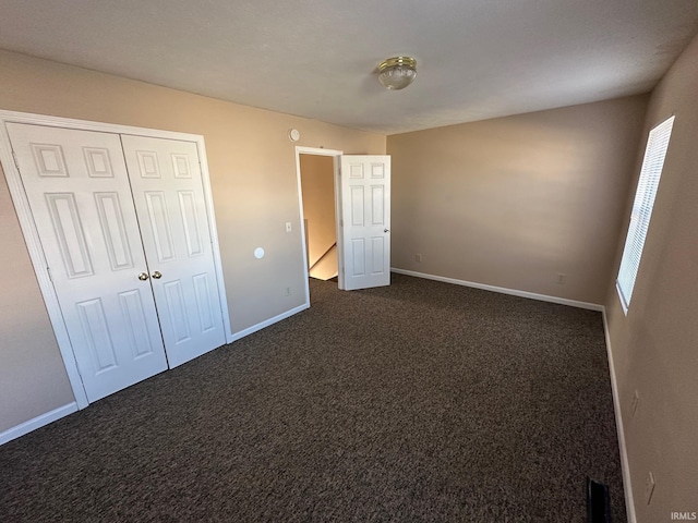 unfurnished bedroom with dark colored carpet and a closet