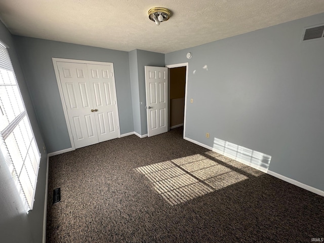 unfurnished bedroom with dark colored carpet, a textured ceiling, and a closet