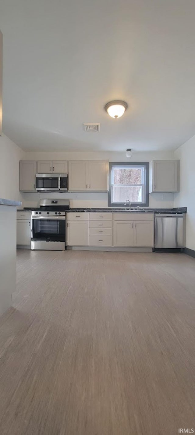 kitchen featuring appliances with stainless steel finishes, light hardwood / wood-style flooring, gray cabinetry, and sink