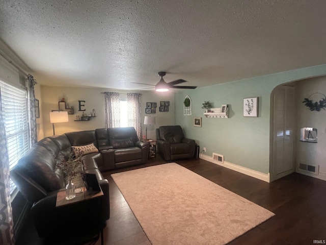 living room featuring ceiling fan, dark wood-type flooring, and a textured ceiling