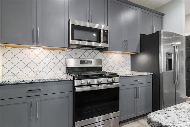 kitchen with decorative backsplash, gray cabinets, light stone counters, and appliances with stainless steel finishes