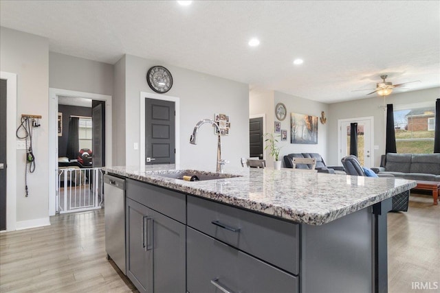 kitchen with ceiling fan, sink, stainless steel dishwasher, light hardwood / wood-style floors, and a center island with sink