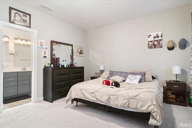 bedroom featuring connected bathroom, sink, light colored carpet, and a textured ceiling