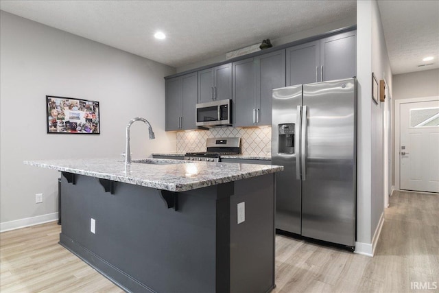 kitchen featuring a kitchen island with sink, sink, light hardwood / wood-style flooring, appliances with stainless steel finishes, and light stone counters