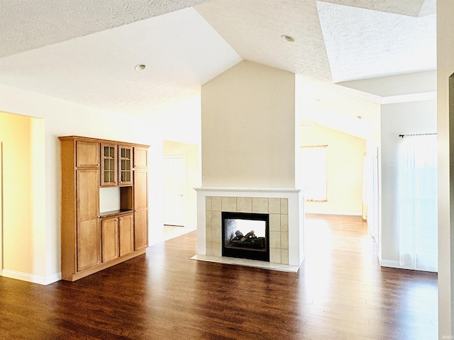 unfurnished living room featuring a textured ceiling, a tiled fireplace, dark hardwood / wood-style floors, and vaulted ceiling