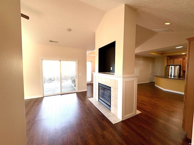 unfurnished living room featuring dark hardwood / wood-style floors, lofted ceiling, and a tiled fireplace