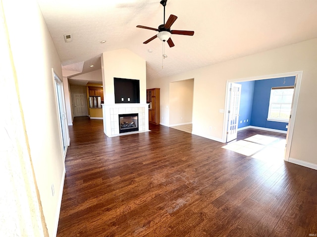 unfurnished living room with a tiled fireplace, ceiling fan, dark wood-type flooring, and vaulted ceiling