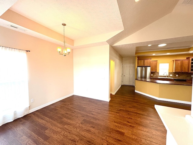 unfurnished living room with sink, a raised ceiling, dark hardwood / wood-style floors, a chandelier, and a textured ceiling