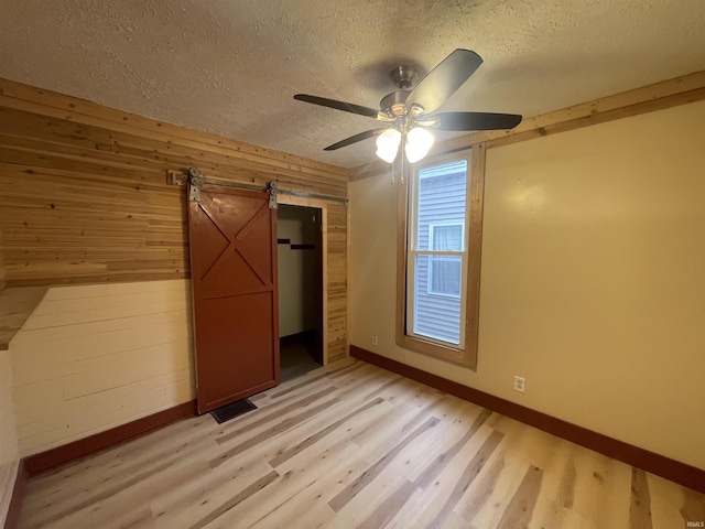 unfurnished bedroom featuring ceiling fan, wood walls, a barn door, and light hardwood / wood-style flooring