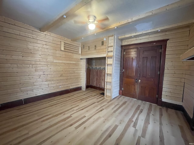 unfurnished bedroom with beamed ceiling, ceiling fan, wooden walls, and light hardwood / wood-style flooring