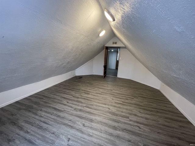 additional living space featuring a textured ceiling, vaulted ceiling, and dark wood-type flooring