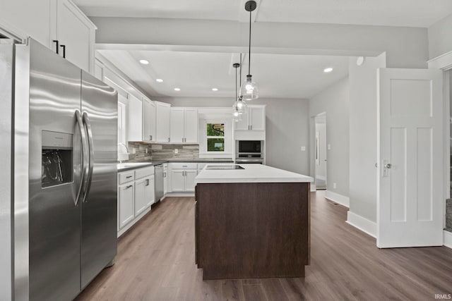 kitchen with backsplash, stainless steel appliances, a center island, white cabinetry, and hanging light fixtures