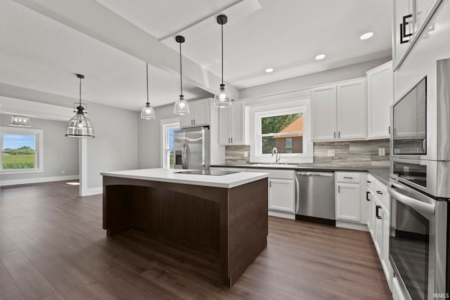 kitchen with hanging light fixtures, stainless steel appliances, a kitchen island, decorative backsplash, and white cabinets