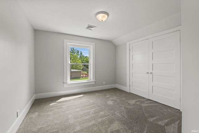 unfurnished bedroom featuring dark colored carpet, a textured ceiling, vaulted ceiling, and a closet