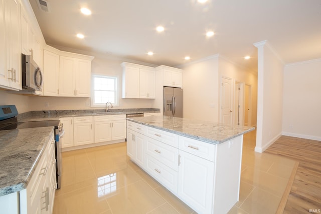 kitchen with white cabinetry, a kitchen island, stainless steel appliances, and light stone counters