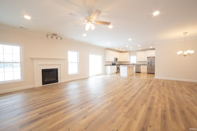 unfurnished living room with a healthy amount of sunlight, light wood-type flooring, ornamental molding, and track lighting