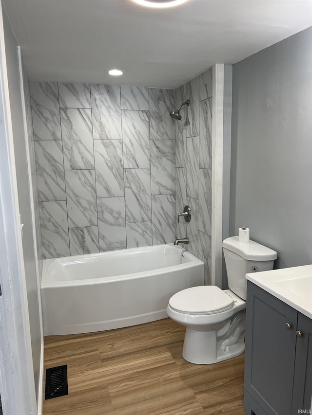 full bathroom with hardwood / wood-style floors, vanity, tiled shower / bath combo, and toilet