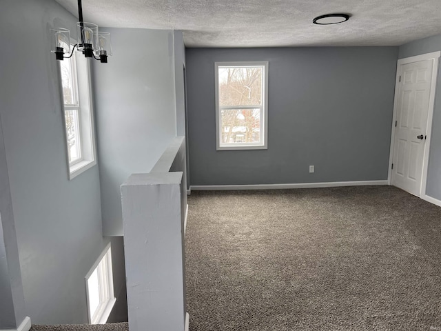 carpeted empty room with a notable chandelier and a textured ceiling