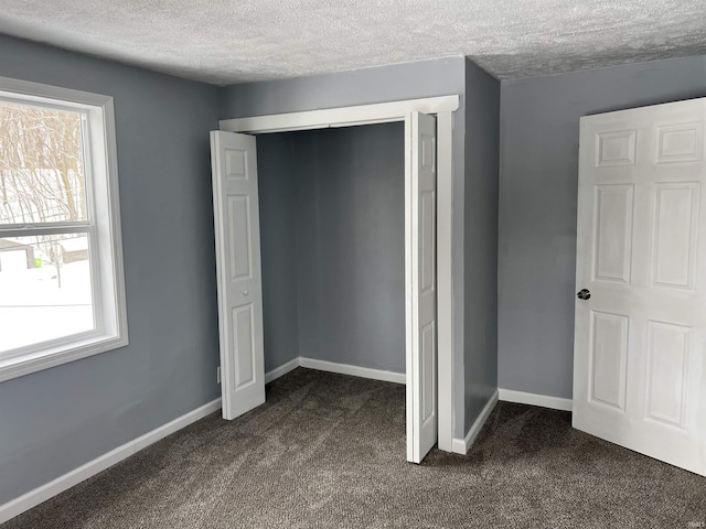 unfurnished bedroom with dark colored carpet, a textured ceiling, and multiple windows