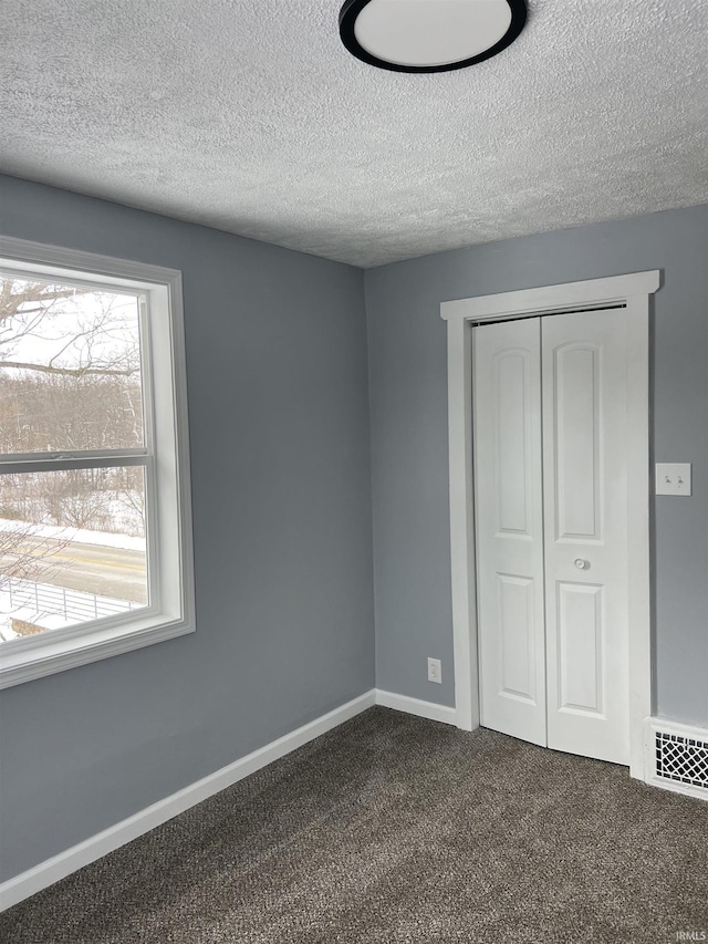 unfurnished bedroom featuring a textured ceiling, dark carpet, and a closet