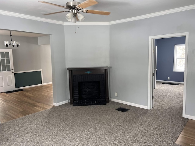 unfurnished living room with a fireplace, ceiling fan with notable chandelier, dark carpet, and crown molding