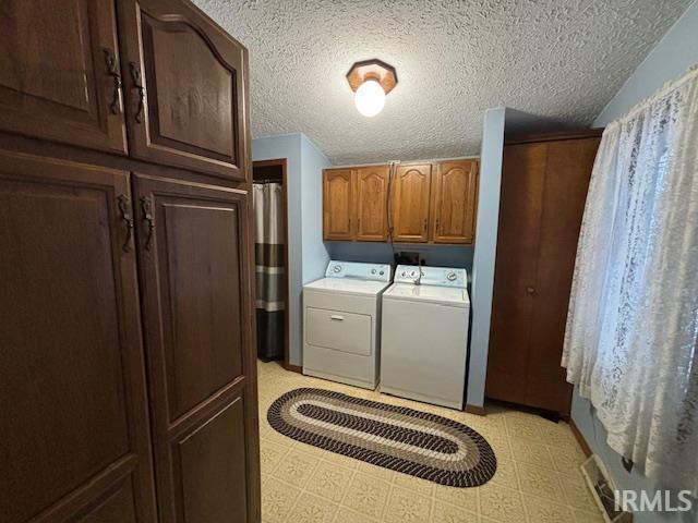 washroom featuring cabinet space, washer and dryer, light floors, and a textured ceiling