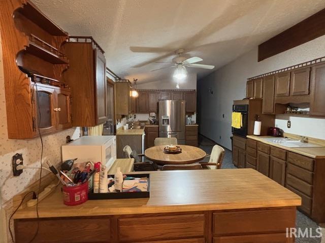 kitchen with oven, vaulted ceiling, ceiling fan, stainless steel fridge, and a textured ceiling