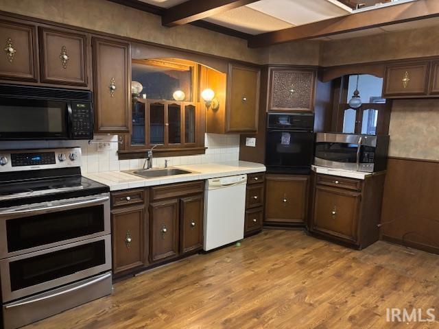 kitchen with black appliances, sink, dark brown cabinetry, and beamed ceiling