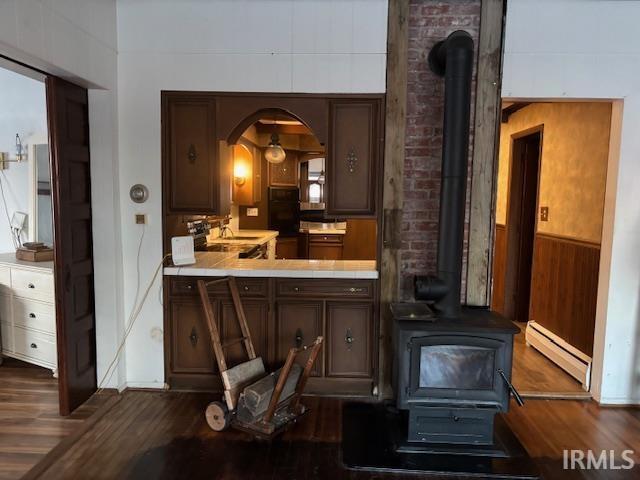 interior space with hardwood / wood-style flooring, a wood stove, wooden walls, and a baseboard radiator