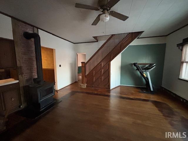 unfurnished living room featuring ceiling fan, dark hardwood / wood-style flooring, a wood stove, and ornamental molding