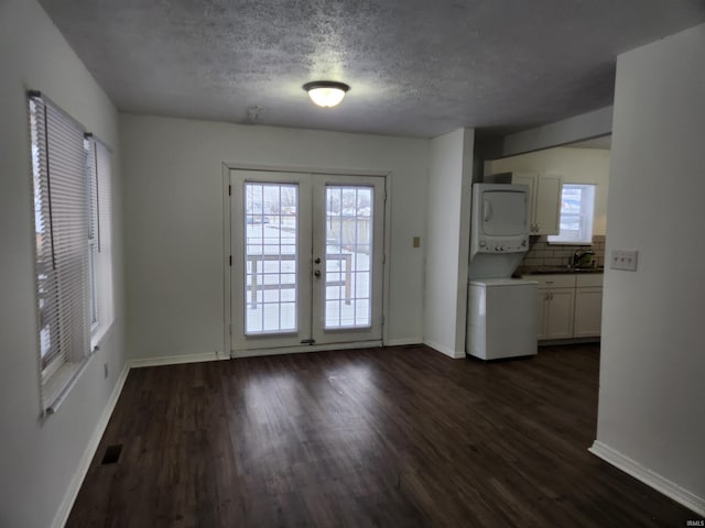 doorway to outside with a textured ceiling, dark hardwood / wood-style floors, stacked washer / dryer, and french doors