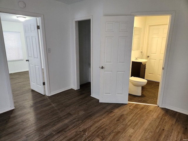 unfurnished bedroom featuring ensuite bathroom, dark wood-type flooring, and sink