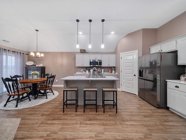 kitchen with white cabinetry, stainless steel appliances, a notable chandelier, decorative light fixtures, and a center island with sink