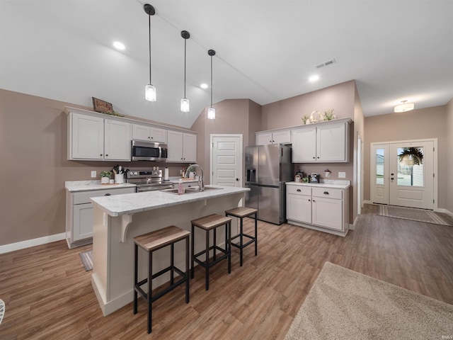 kitchen featuring a breakfast bar, stainless steel appliances, a center island with sink, white cabinets, and hanging light fixtures