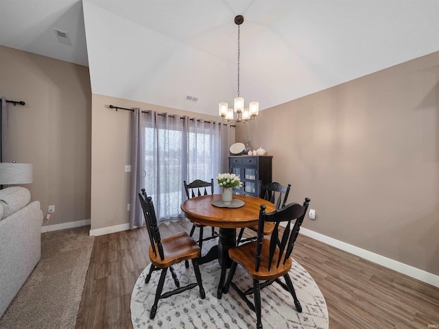 dining space featuring hardwood / wood-style flooring, vaulted ceiling, and an inviting chandelier