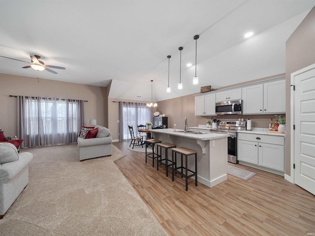 kitchen featuring lofted ceiling, a kitchen island with sink, white cabinets, appliances with stainless steel finishes, and decorative light fixtures