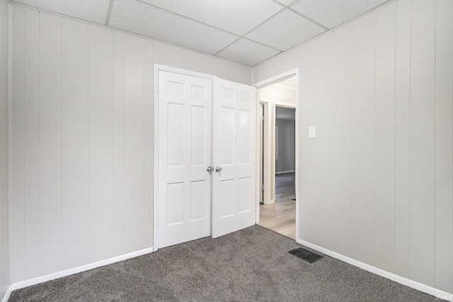 unfurnished bedroom featuring a closet, a drop ceiling, and carpet