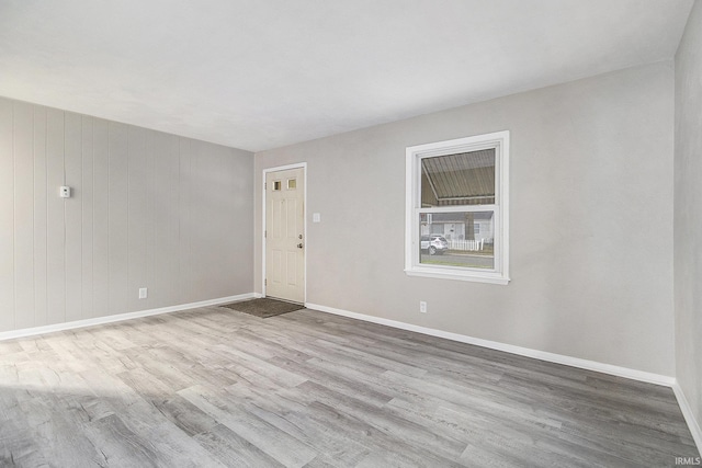 unfurnished room featuring light wood-type flooring and wooden walls