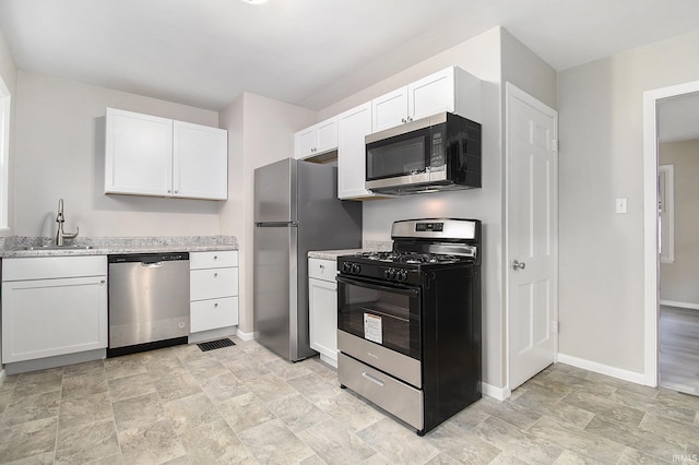 kitchen featuring white cabinetry, sink, light stone counters, and appliances with stainless steel finishes