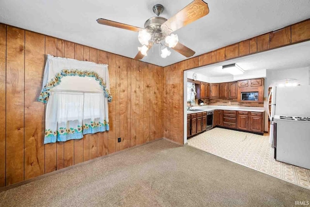 kitchen with wood walls, light carpet, ceiling fan, built in microwave, and dishwashing machine