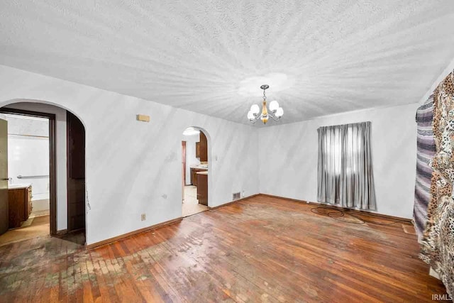 empty room with wood-type flooring, a textured ceiling, and an inviting chandelier