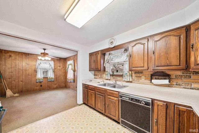 kitchen featuring ceiling fan, dishwasher, sink, wood walls, and light carpet