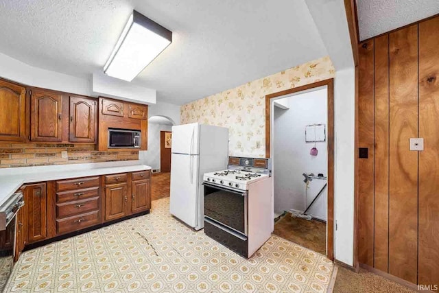 kitchen with a textured ceiling, wooden walls, and white appliances