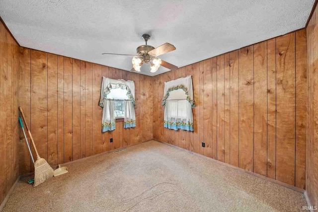 empty room with a textured ceiling, carpet floors, and wood walls