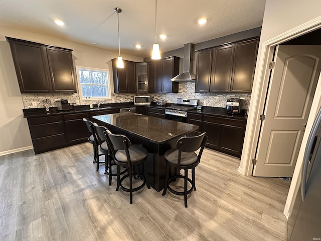 kitchen featuring hanging light fixtures, light hardwood / wood-style flooring, wall chimney exhaust hood, a kitchen island, and stainless steel appliances