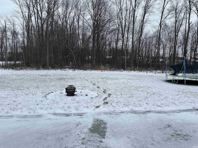 yard layered in snow featuring a trampoline and a fire pit