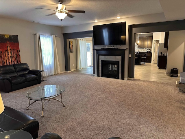 living room with ceiling fan, light colored carpet, a textured ceiling, and a tile fireplace